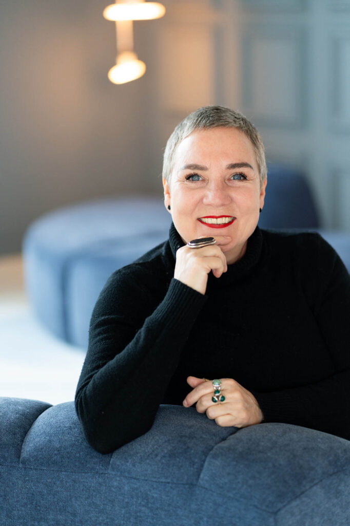 Vrouw met een brede lach en kijkt recht in de camera.