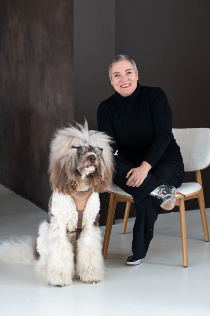 Vrouw zit op een stoel en een hond heeft een bril op.